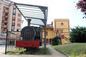 Locomotora de vapor SHE 11, al fondo la Antigua Estación del Ferrocarril Vasco Asturiana